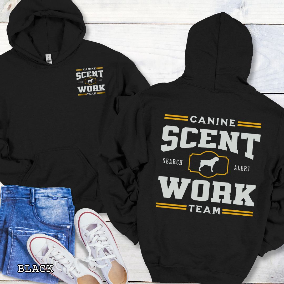 Black back print hoodie with 'Canine Scent Work Team' text on a wooden surface.