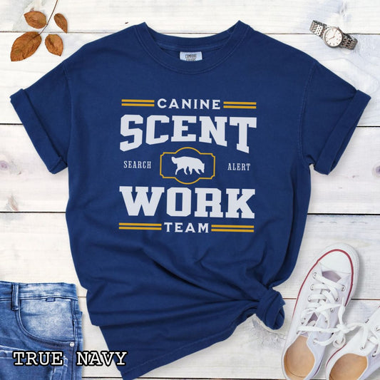 Navy blue Comfort Colors t-shirt with 'Canine Scent Work Team' and custom breed silhouette, presented text on a wooden surface with shoes and jeans.