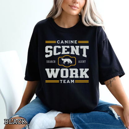 Black Comfort Colors t-shirt with 'Canine Scent Work Team' and custom breed silhouette, presented text on a wooden surface with shoes and jeans.