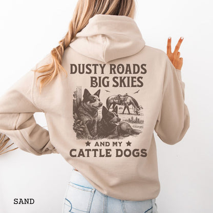 Back view of sand-beige Blue Heeler hoodie featuring a Western-style design with grazing horse, rustic fence, and Cattle Dog illustration; text reads “Dusty Roads, Big Skies, and My Cattle Dogs.”