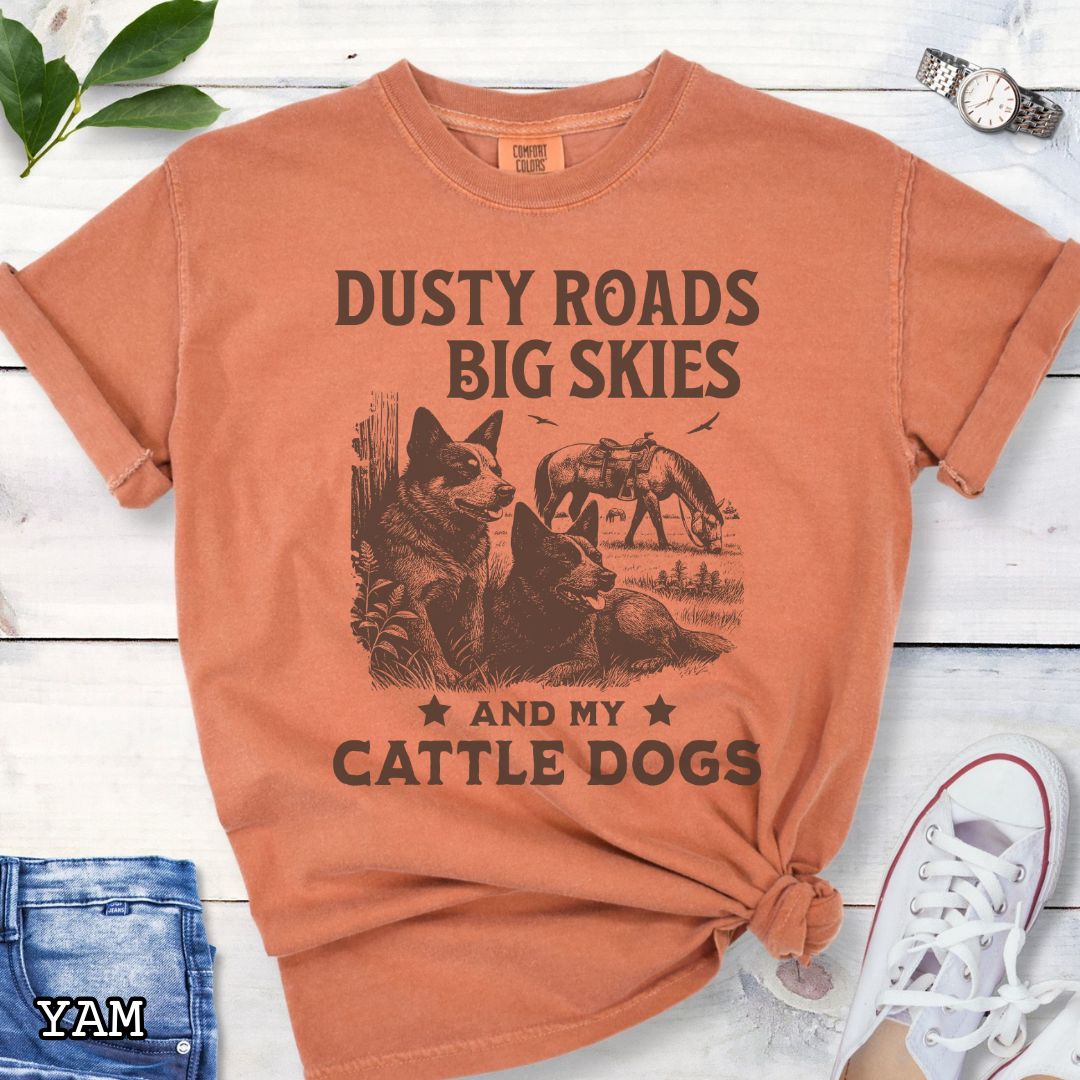 Yam-orange Comfort Colors Cattle Dog t-shirt featuring a Western-style design with grazing horse, rustic fence, and Cattle Dog illustration; text reads “Dusty Roads, Big Skies, and My Cattle Dogs.”