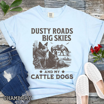 Light blue Comfort Colors Cattle Dog t-shirt featuring a Western-style design with grazing horse, rustic fence, and Cattle Dog illustration; text reads “Dusty Roads, Big Skies, and My Cattle Dogs.”