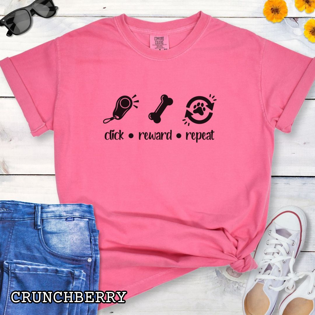 Pink Comfort Colors t-shirt featuring a Click Reward Repeat design with clicker, treat, and paw graphics for positive reinforcement dog trainers and clicker training enthusiasts.