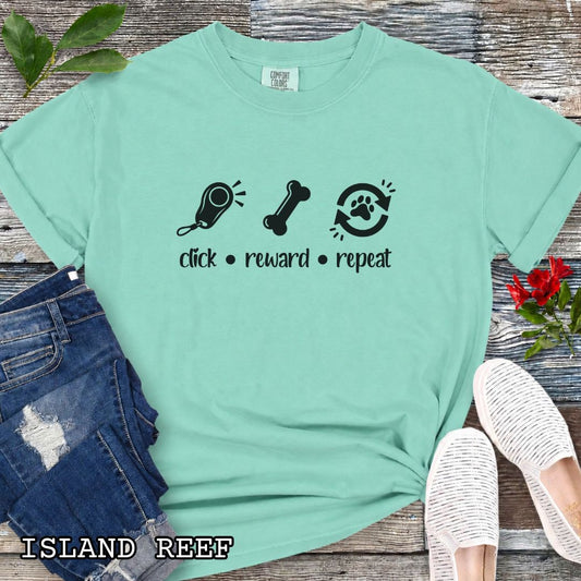 Teal green Comfort Colors t-shirt featuring a Click Reward Repeat design with clicker, treat, and paw graphics for positive reinforcement dog trainers and clicker training enthusiasts.