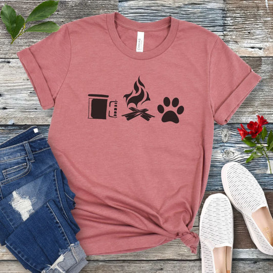 A mauve camping and dogs t-shirt with graphics of a coffee cup, campfire, and dog paw print, accompanied by rolled-up blue jeans and white sneakers on a wooden surface.