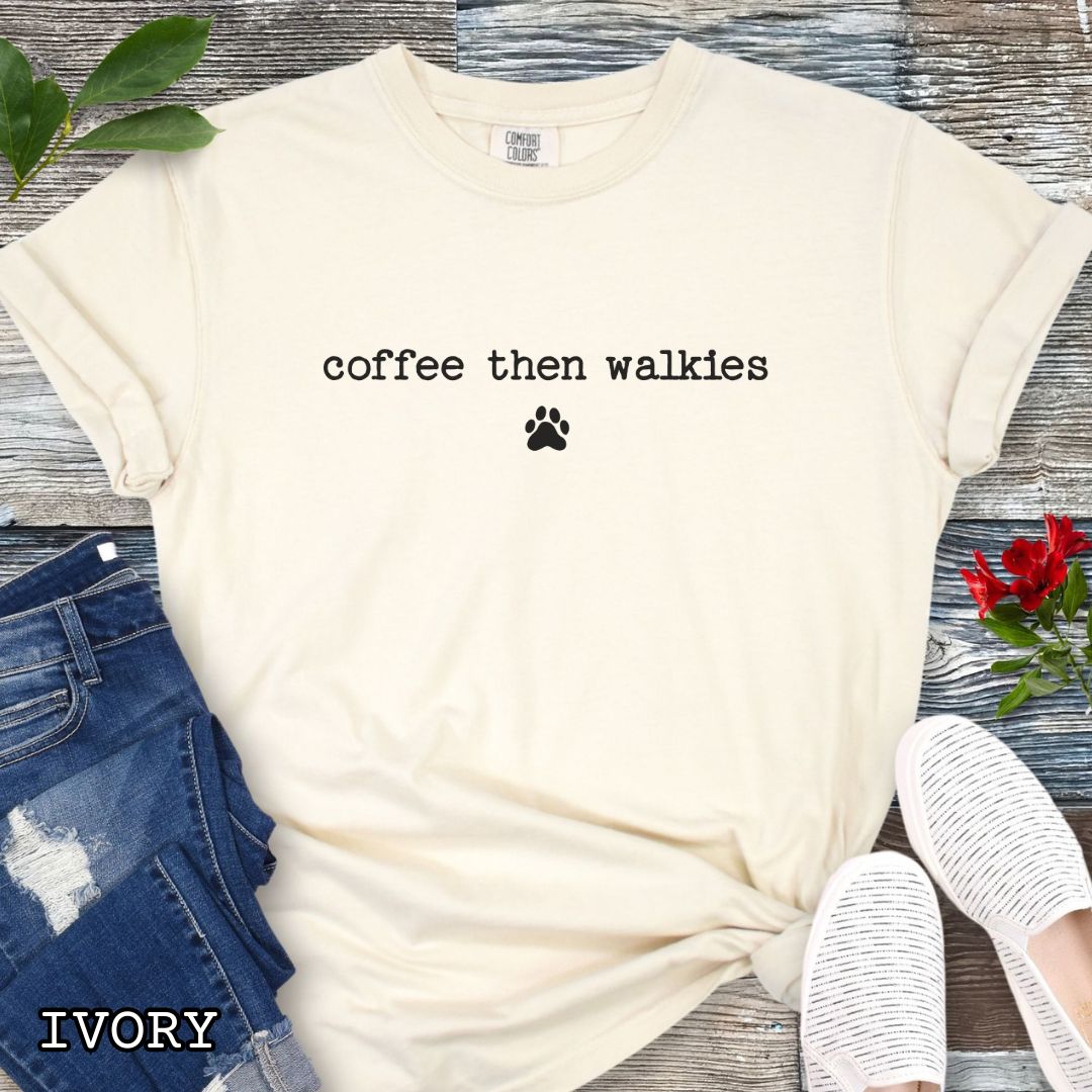 Beige Comfort Colors t-shirt for coffee loving dog owners with funny text 'coffee then walkies', shown on a white wooden surface with shoes and jeans.