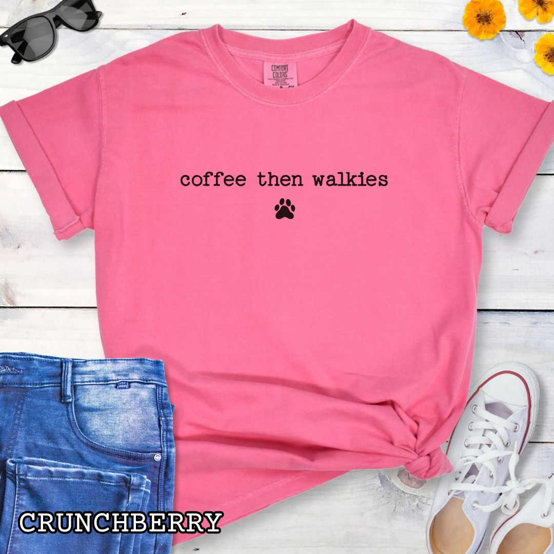 Pink Comfort Colors t-shirt for coffee loving dog owners with funny text 'coffee then walkies', shown on a white wooden surface with shoes and jeans.