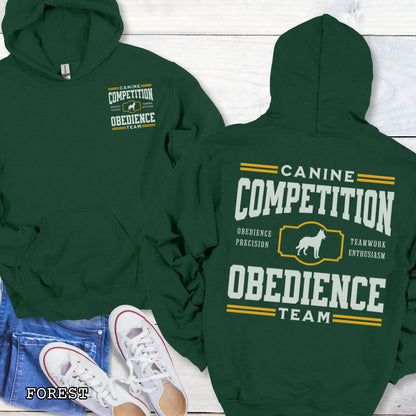 Green dog obedience back print hoodie with 'Canine Competition Obedience Team' text and custom breed silhouette, presented on a wooden surface with denim jeans and a flower.