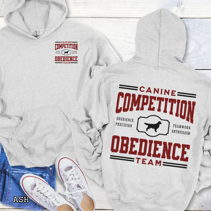 Light grey dog obedience back print hoodie with 'Canine Competition Obedience Team' text and custom breed silhouette, presented on a wooden surface with denim jeans and a flower.
