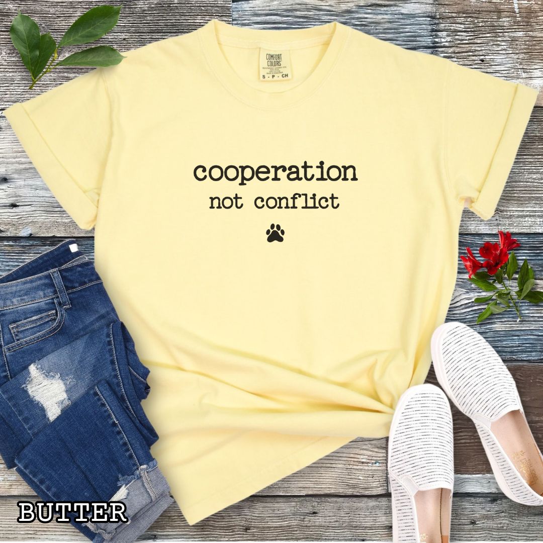 Yellow (Butter) Comfort Colors dog training t-shirt with 'cooperation not conflict' text on a wooden surface with shoes and jeans.