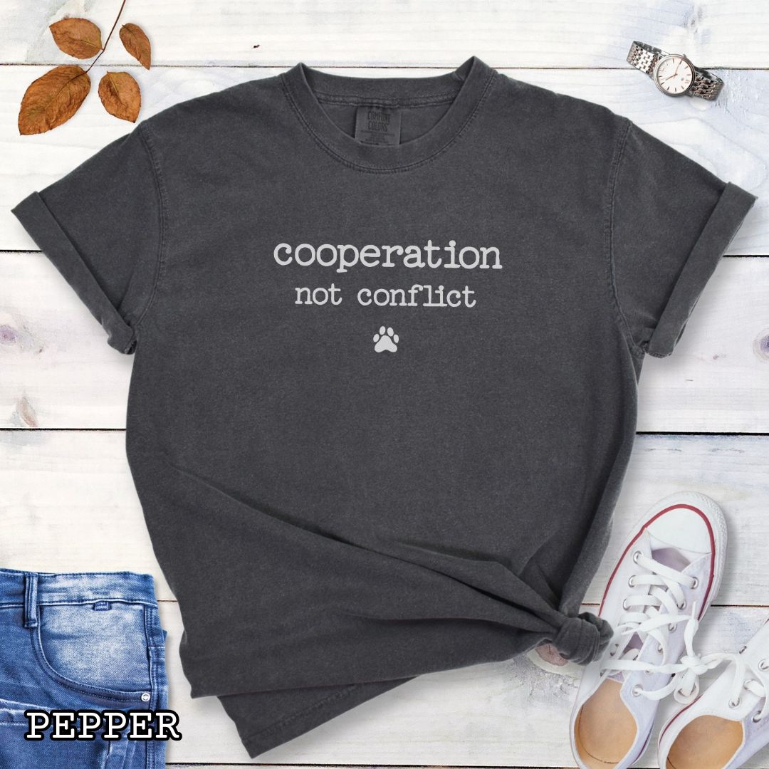 Dark gray (Pepper) Comfort Colors dog training t-shirt with 'cooperation not conflict' text on a wooden surface with shoes and jeans.