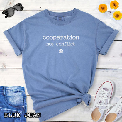 Blue Jean color Comfort Colors dog training t-shirt with 'cooperation not conflict' text on a wooden surface with shoes and jeans.
