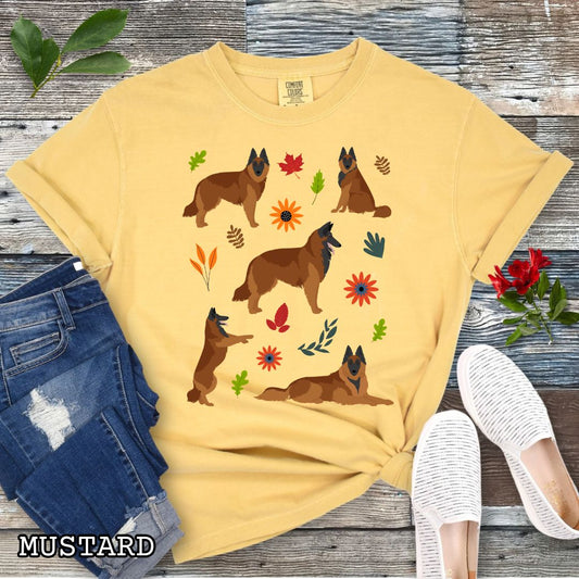 Yellow Comfort Colors t-shirt with Belgian Tervuren dog illustrations accented by colorful fall flowers and foliage, shown on a wooden surface with jeans and shoes.