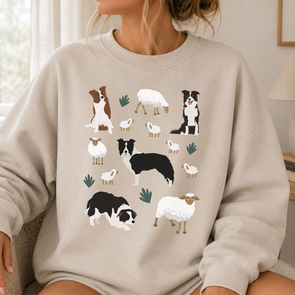 A woman wearing a light beige crewneck sweatshirt with a graphic print of various Border Collie dogs and sheep in black, white, and brown, set against a soft-focus indoor background.