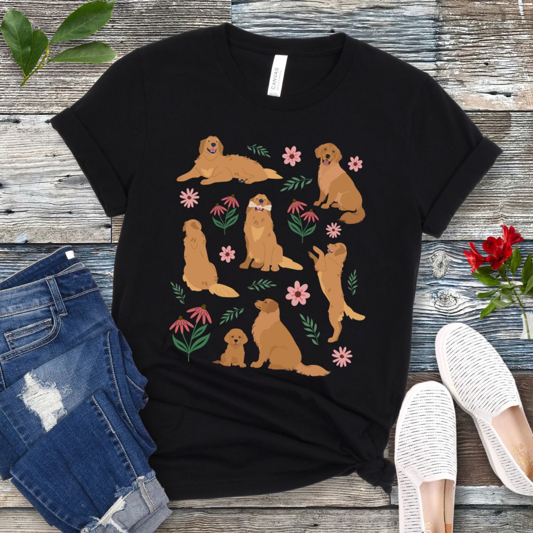Black dog lover t-shirt with cottagecore-style design made of Golden Retriever dogs in various positions, accented by flowers and leaves, shown on a wooden surface with jeans and shoes.