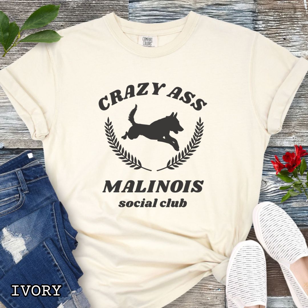 Beige Comfort Colors t-shirt with funny Crazy Ass Malinois Social Club design with jumping Belgian Malinois silhouette, perfect gift for Malinois owners, dog trainers, K9 handlers, working dog fans, and protection sport enthusiasts.