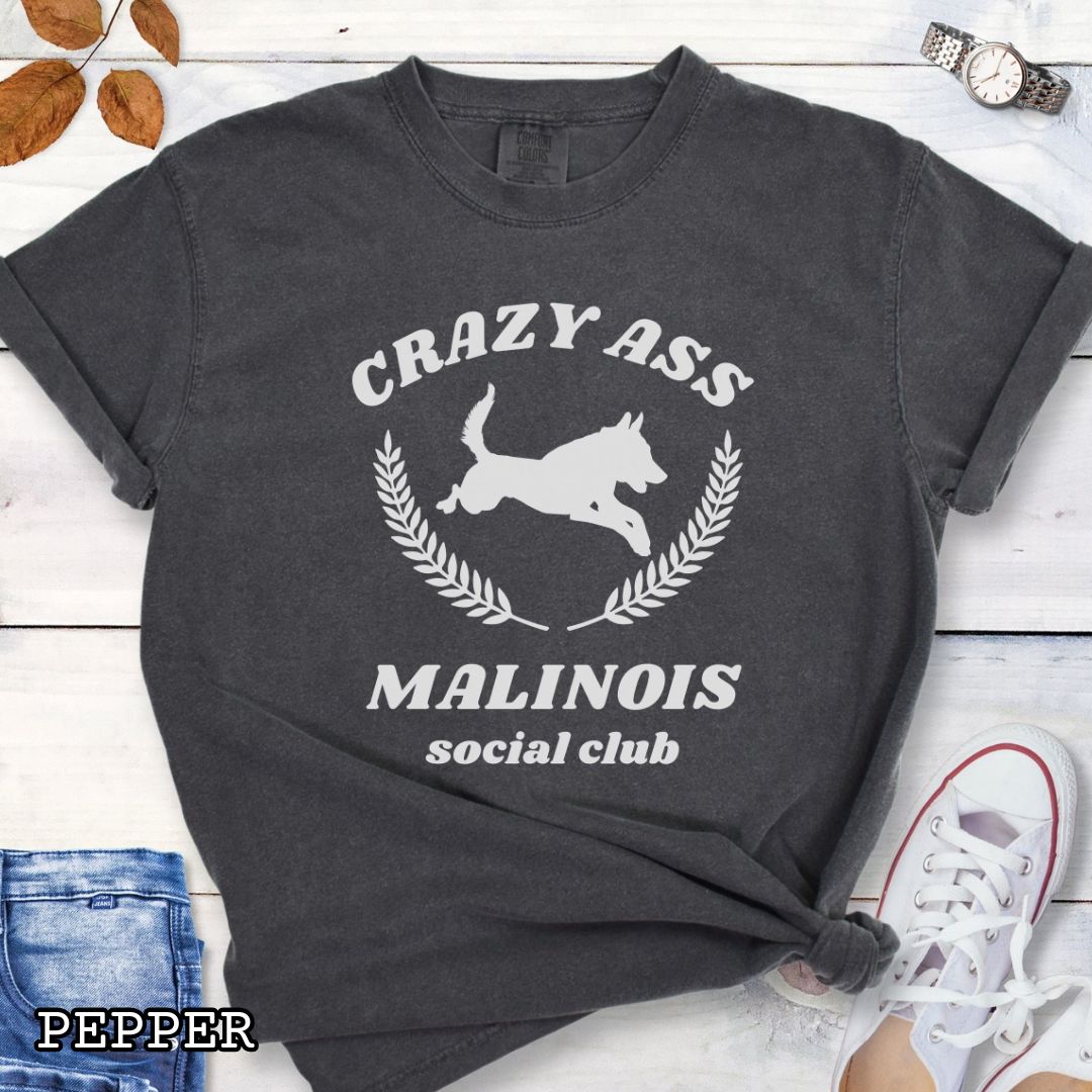 Dark grey Comfort Colors t-shirt with funny Crazy Ass Malinois Social Club design with jumping Belgian Malinois silhouette, perfect gift for Malinois owners, dog trainers, K9 handlers, working dog fans, and protection sport enthusiasts.