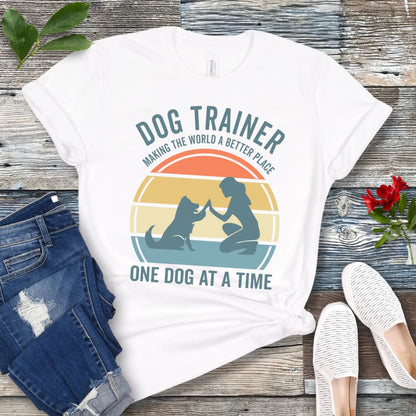 White t-shirt with 'Dog Trainer' graphic and positive quote on a wooden surface with jeans and shoes.