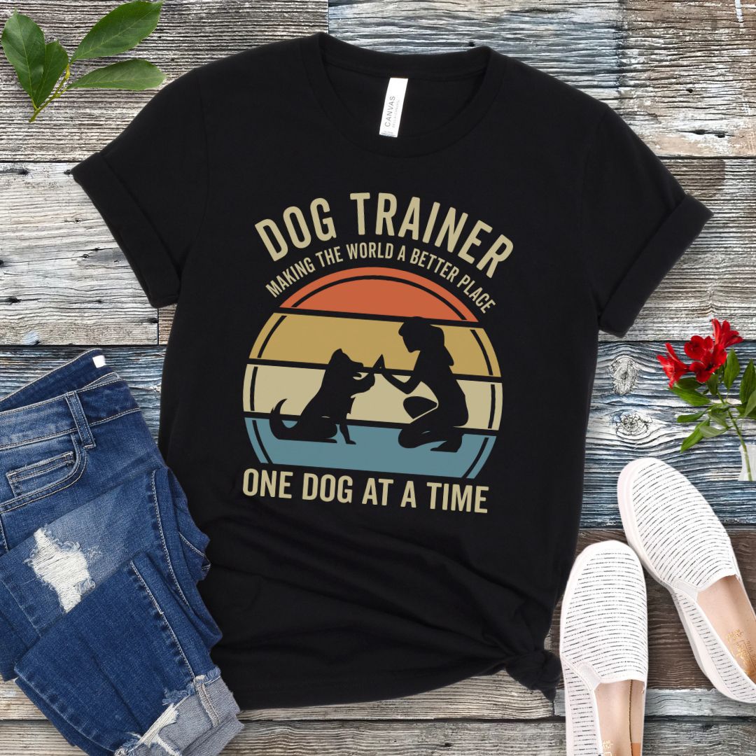 Black t-shirt with 'Dog Trainer' graphic and positive quote on a wooden surface with jeans and shoes.