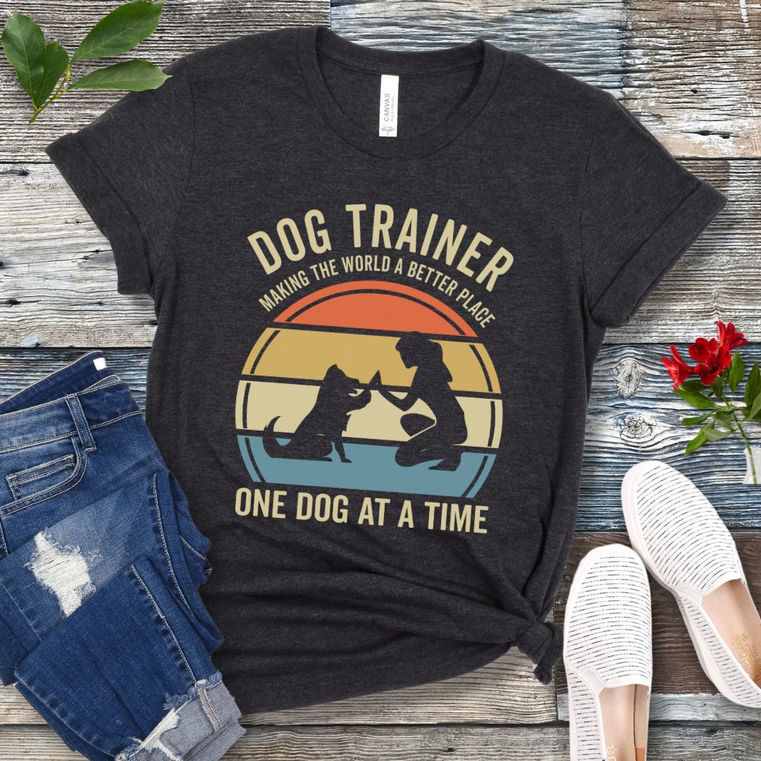 Dark grey t-shirt with 'Dog Trainer' graphic and positive quote on a wooden surface with jeans and shoes.