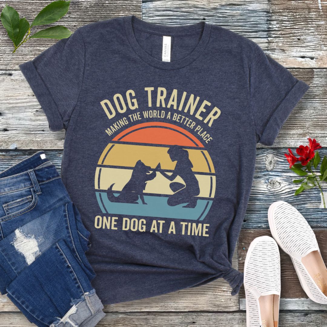 Heather navy blue t-shirt with 'Dog Trainer' graphic and positive quote on a wooden surface with jeans and shoes.