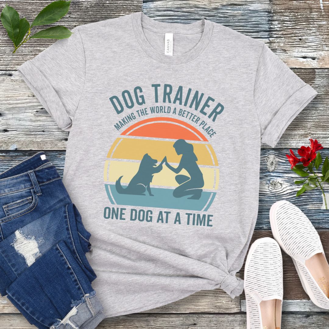 Light grey t-shirt with 'Dog Trainer' graphic and positive quote on a wooden surface with jeans and shoes.