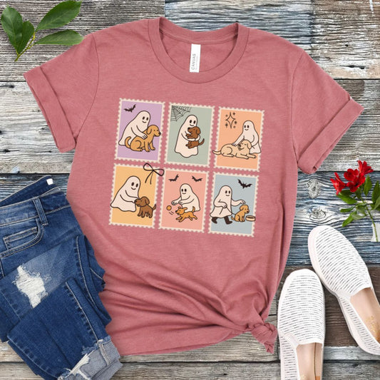Mauve t-shirt for spooky dog lovers with cartoon ghosts and dogs in a postage stamp style design, shown on a wooden surface with jeans and shoes.