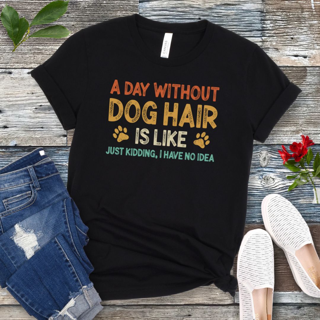 Black t-shirt with colorful text 'A day without DOG HAIR is like, just kidding, I have no idea', presented on a wooden surface with jeans and casual shoes.