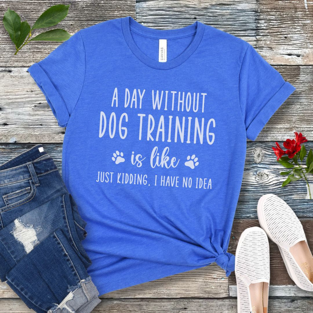Royal blue unisex t-shirt with humorous dog training quote, 'A Day Without Dog Training Is Like, Just Kidding, I have No Idea' text, presented on a wooden surface with jeans and shoes.