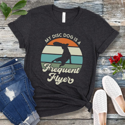 Dark grey unisex disc dog t-shirt with colorful vintage sunset, leaping dog catching a disc, and the humorous text 'My Disc dog is a frequent flyer'. 