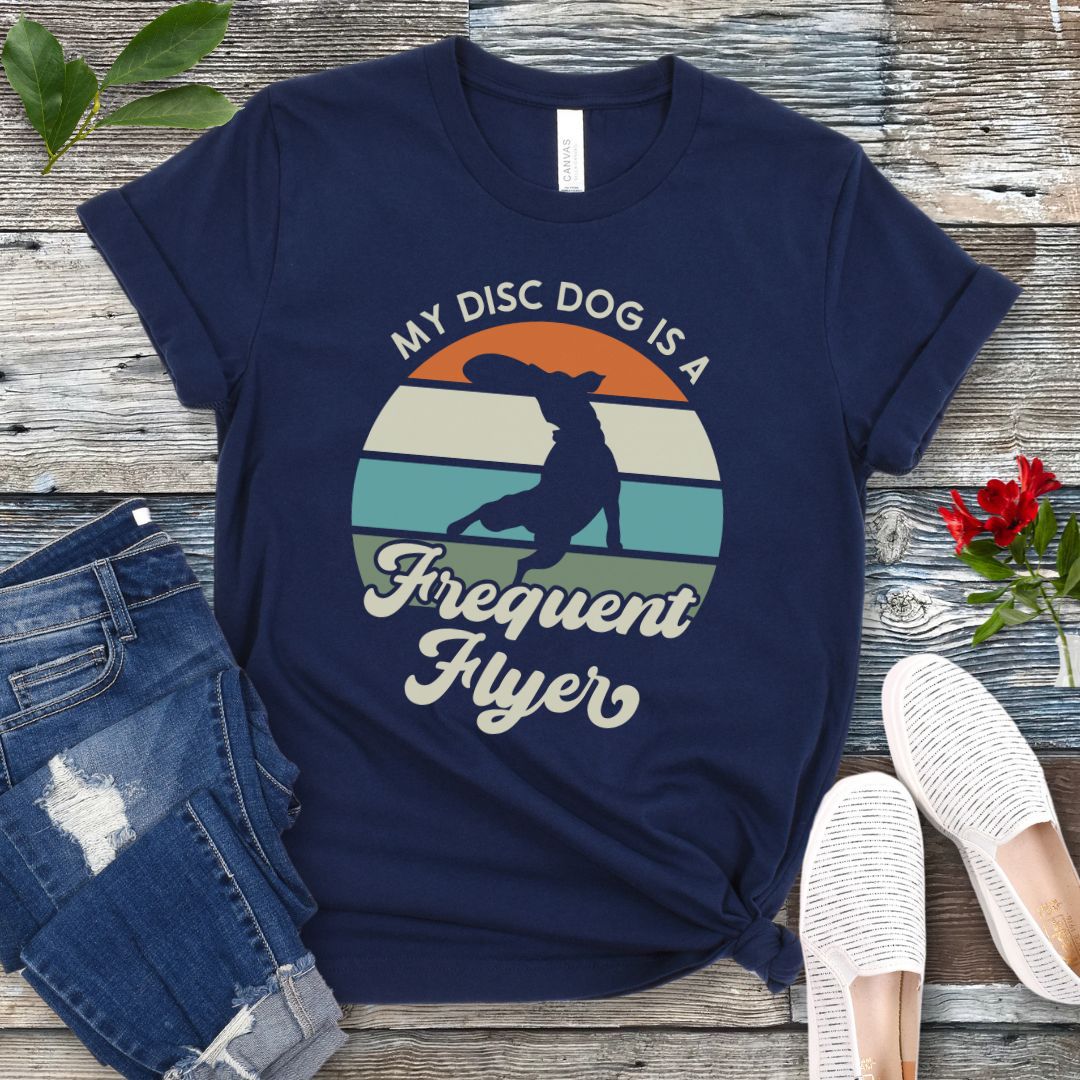 Navy unisex disc dog t-shirt with colorful vintage sunset, leaping dog catching a disc, and the humorous text 'My Disc dog is a frequent flyer'. 