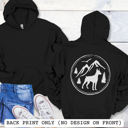 Two black hoodies laid flat on a white wood background, with the front view on the left and back view on the right. The back hoodie has a large white circular mountain-and-dog graphic.