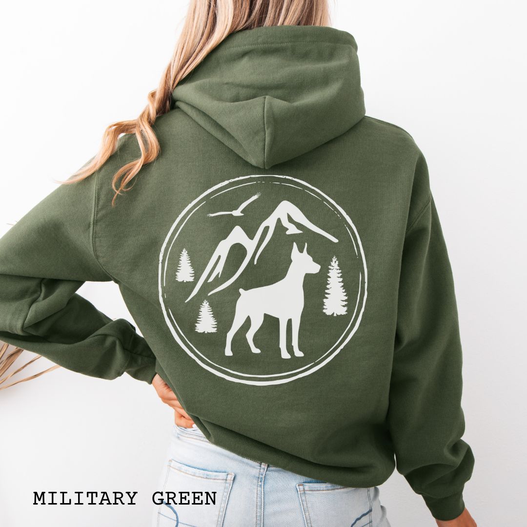 Military Green Doberman Pinscher hoodie featuring a bold vintage-style back print with Doberman silhouette, mountains, pine trees, perfect gift for hiking and outdoorsy Doberman dog lovers.