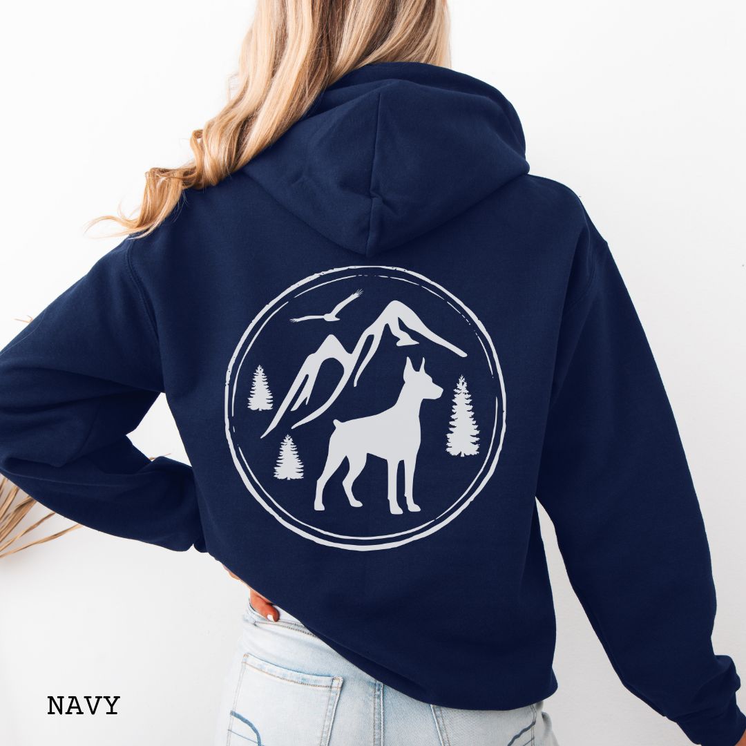 Navy blue Doberman Pinscher hoodie featuring a bold vintage-style back print with Doberman silhouette, mountains, pine trees, perfect gift for hiking and outdoorsy Doberman dog lovers.