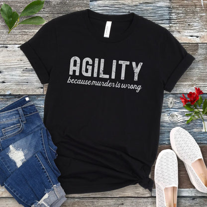 Black t-shirt with 'AGILITY because murder is wrong' text on a wooden surface with jeans and shoes.