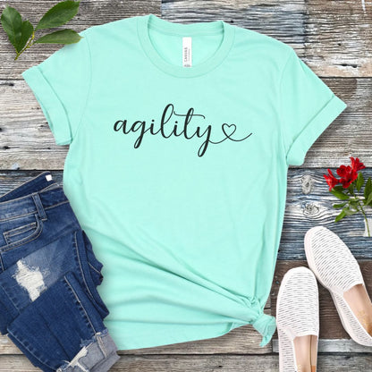 Mint green dog agility t-shirt with 'agility' in handwritten script on a wooden surface with jeans and shoes.