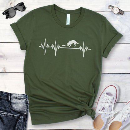 Military green dog scent training t-shirt with a heart rate monitor design featuring a nosework dog sniffing, presented with accessories, jeans, and shoes on a wooden surface.