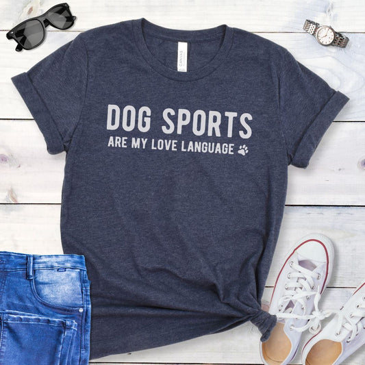 Heather navy t-shirt with 'Dog Sports are my love language' text on a wooden surface with jeans and shoes.