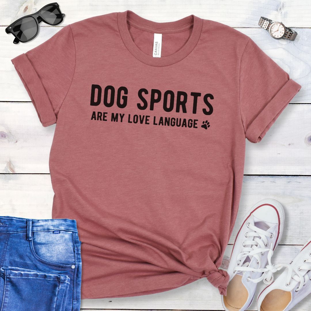 Mauve t-shirt with 'Dog Sports are my love language' text on a wooden surface with jeans and shoes.