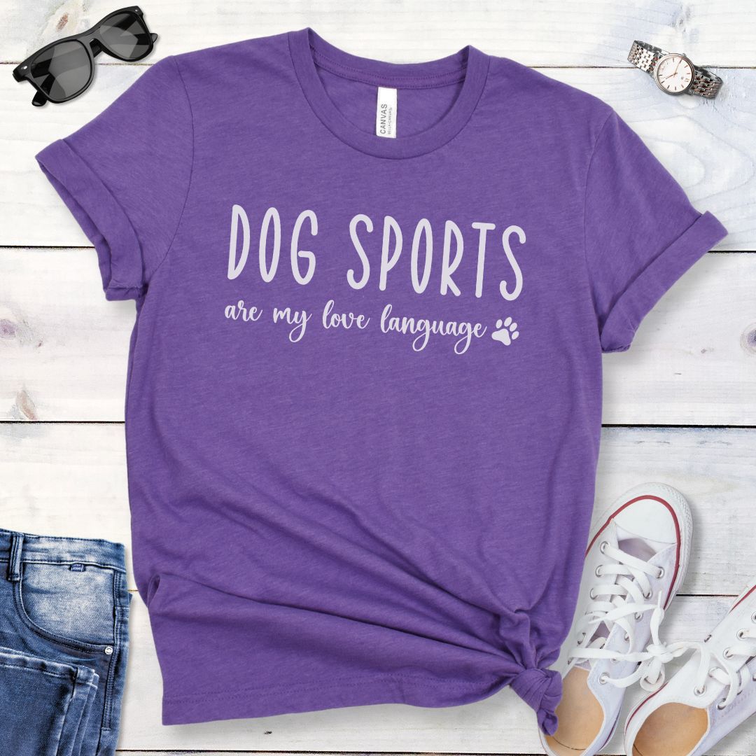 Purple dog training t-shirt with 'Dog Sports are my love language' text on a wooden surface with jeans and shoes.