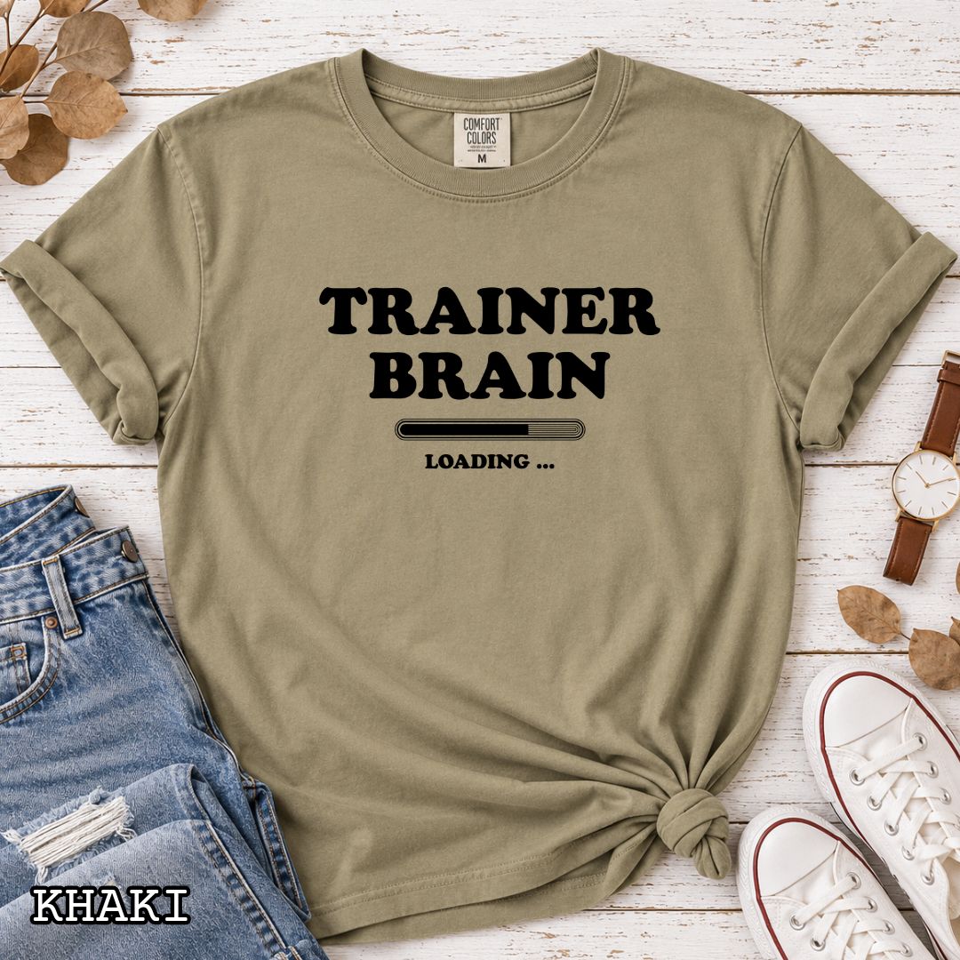 A khaki Comfort Colors unisex t-shirt for dog training enthusiasts, featuring a black text design that reads 'TRAINER BRAIN' above a loading bar and 'LOADING . Makes a perfect funny dog trainer gift.
