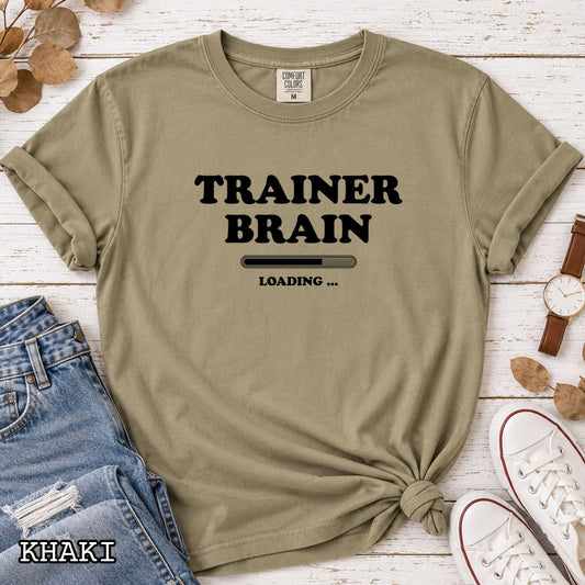 A khaki Comfort Colors unisex t-shirt for dog training enthusiasts, featuring a black text design that reads 'TRAINER BRAIN' above a loading bar and 'LOADING . Makes a perfect funny dog trainer gift.
