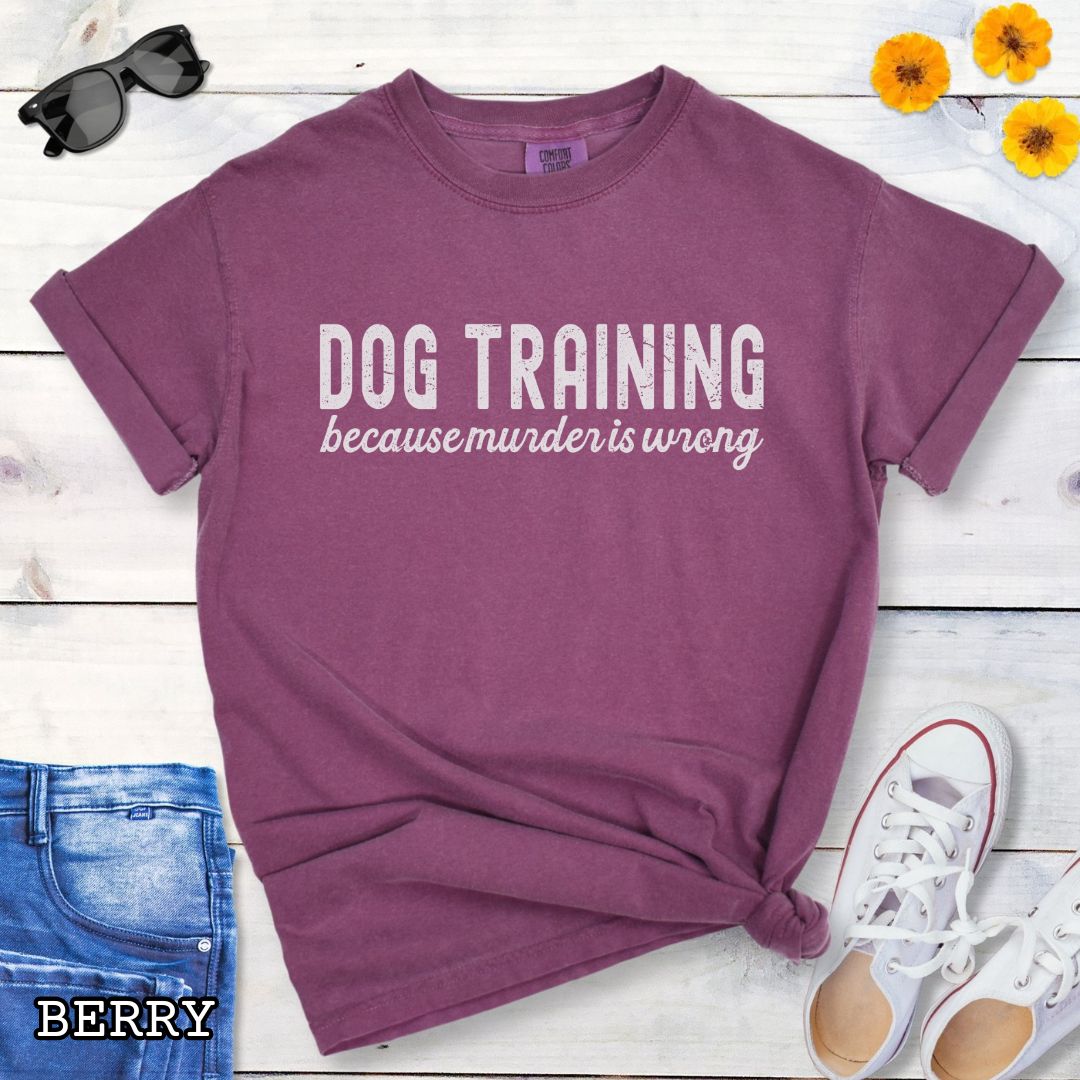 Berry color Comfort Colors t-shirt with 'Dog Training because murder is wrong' text on a wooden surface with sunglasses, jeans, and sneakers.
