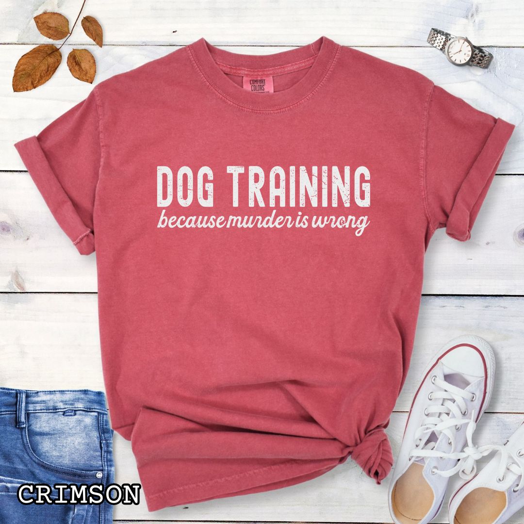 Red (Crimson) Comfort Colors t-shirt with 'Dog Training because murder is wrong' text on a wooden surface with sunglasses, jeans, and sneakers.