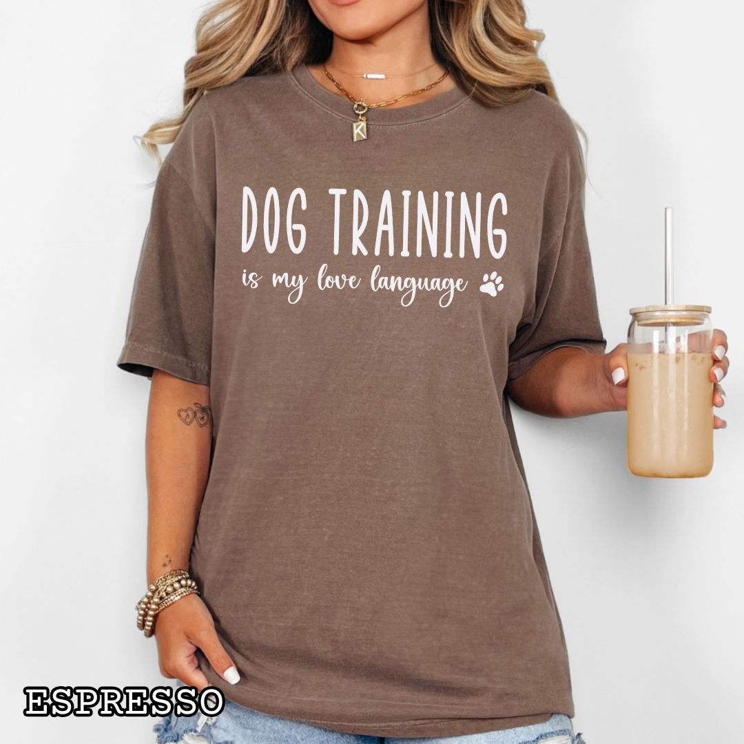 Person wearing a brown (Espresso) Comfort Colors t-shirt with 'Dog training is my love language' text, and a small paw print, holding a drink.
