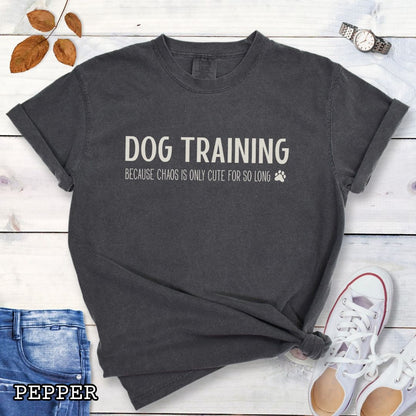 Dark grey (Pepper) Comfort Colors t-shirt with 'Dog Training, Because Chaos is Only Cute For So Long' text and a small paw print, on a wooden surface with jeans and sneakers.
