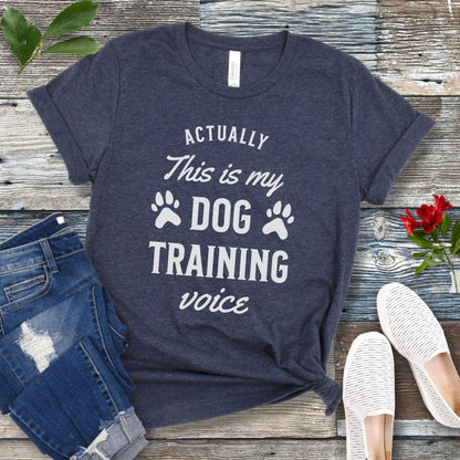 Navy blue t-shirt with 'Dog Training Voice' text on a wooden surface with jeans and shoes.