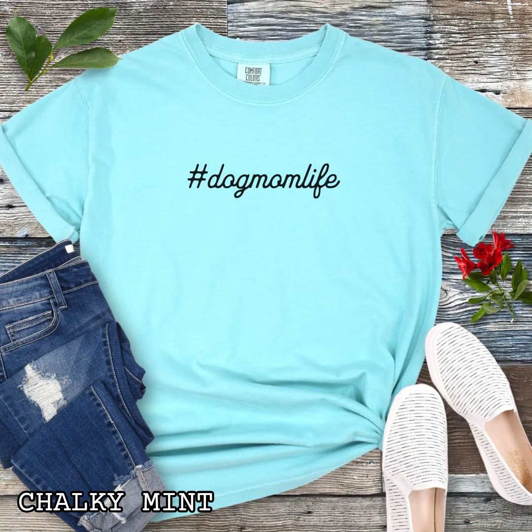Mint Comfort Colors t-shirt for dog lovers with '#dogmomlife' text, shown on a wooden surface with shoes and jeans. 