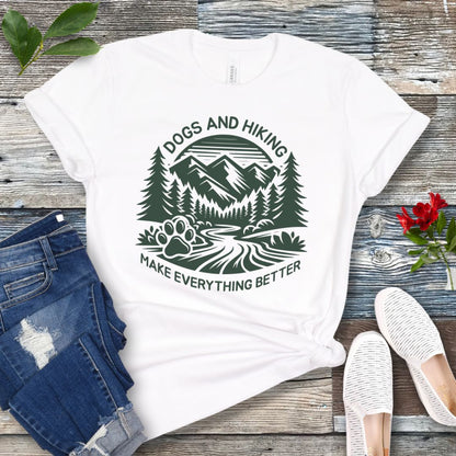 White t-shirt with mountains graphic with paw print and the text 'Dogs and Hiking Make Everything Better', shown on a wooden surface with jeans and shoes.