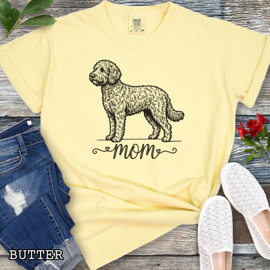 Yellow Comfort Colors t-shirt for Doodle dog moms with a vintage-style Doodle dog illustration and 'mom' text in script lettering beneath it, shown on a wooden surface with jeans and shoes.